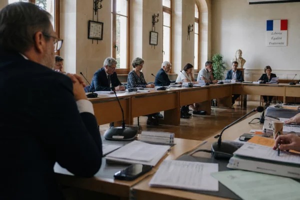 Salle municipale française avec chaise vide, micros et dossiers flous dans une ambiance politique calme.