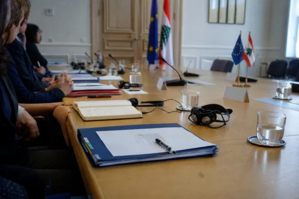 Table de négociation européenne avec dossiers, écouteurs et drapeaux miniatures, dans une salle diplomatique lumineuse.