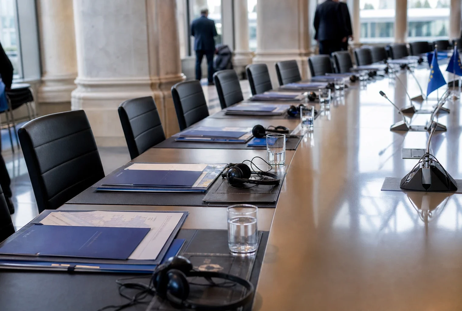 Table de négociation européenne avec casques, dossiers et petits drapeaux UE discrets dans une salle de Bruxelles.
