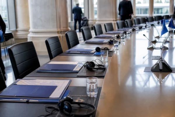 Table de négociation européenne avec casques, dossiers et petits drapeaux UE discrets dans une salle de Bruxelles.