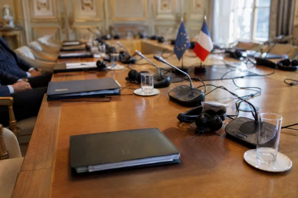 Table de négociation avec dossiers, micros et silhouettes anonymes dans une salle institutionnelle lumineuse