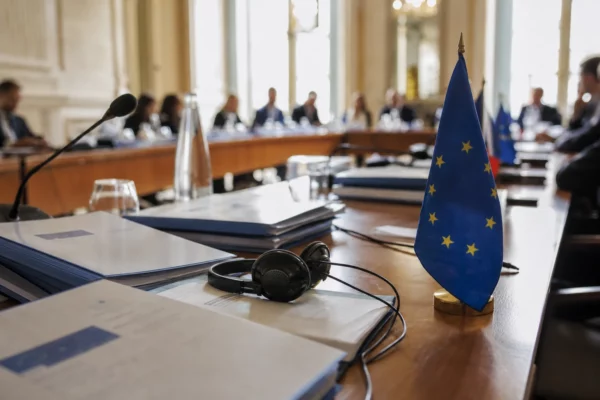 Table de négociation européenne avec dossiers, écouteurs et petits drapeaux de l’UE dans une salle institutionnelle lumineuse.