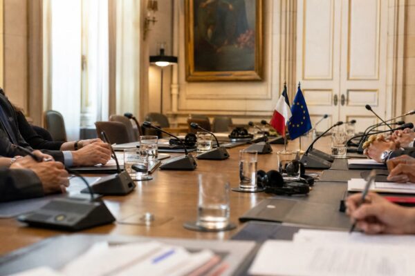 Réunion diplomatique à Paris avec dossiers fermés, micros et petits drapeaux discrets sur une table de négociation.