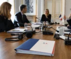 Table de négociation diplomatique avec dossiers, micros et petits drapeaux français et britannique, dans une salle institutionnelle claire.