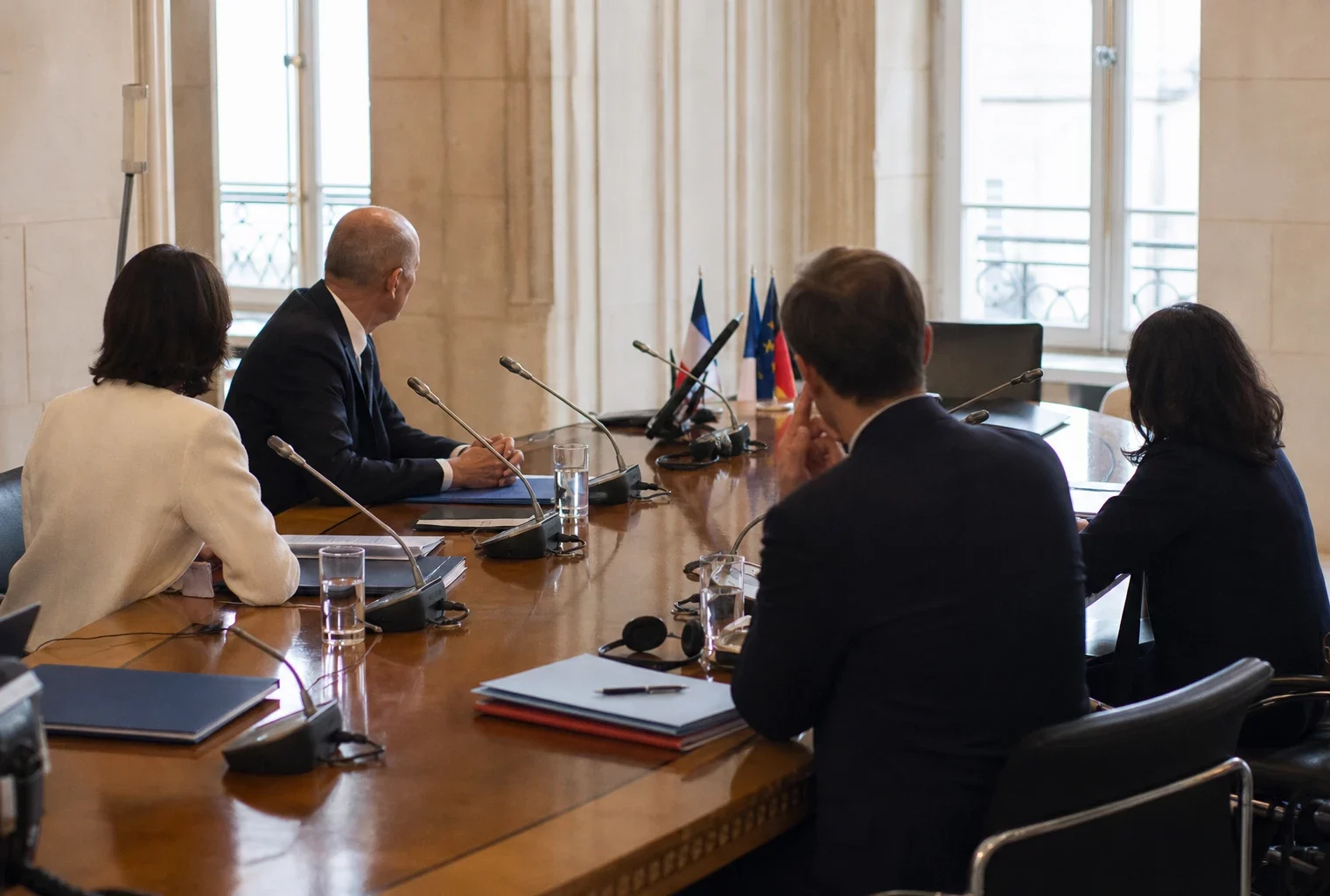 Table de négociation institutionnelle avec dossiers, micros et silhouettes anonymes dans une salle claire