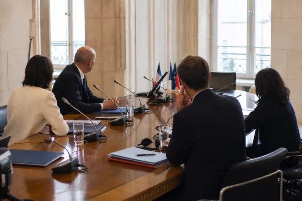 Table de négociation institutionnelle avec dossiers, micros et silhouettes anonymes dans une salle claire