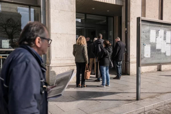Scène de rue française devant un bâtiment municipal, passants anonymes et ambiance civique calme en plein jour