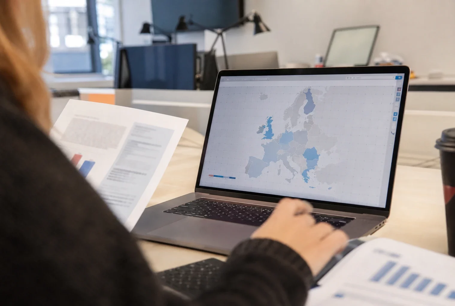 Vue sur l’épaule d’un journaliste devant un ordinateur affichant une interface européenne abstraite, dans un bureau lumineux.