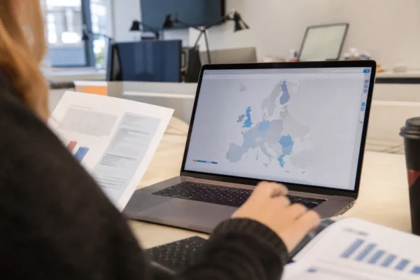 Vue sur l’épaule d’un journaliste devant un ordinateur affichant une interface européenne abstraite, dans un bureau lumineux.