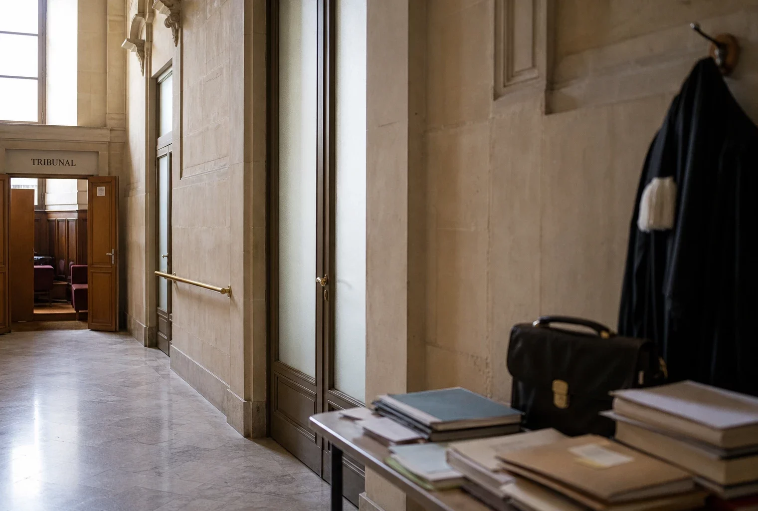 Couloir lumineux d’un tribunal français, avec porte de salle d’audience entrouverte et marbre clair.