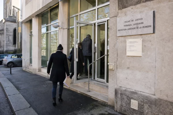 Devant un tribunal français, des silhouettes anonymes entrent dans un bâtiment public sous une lumière de jour claire.