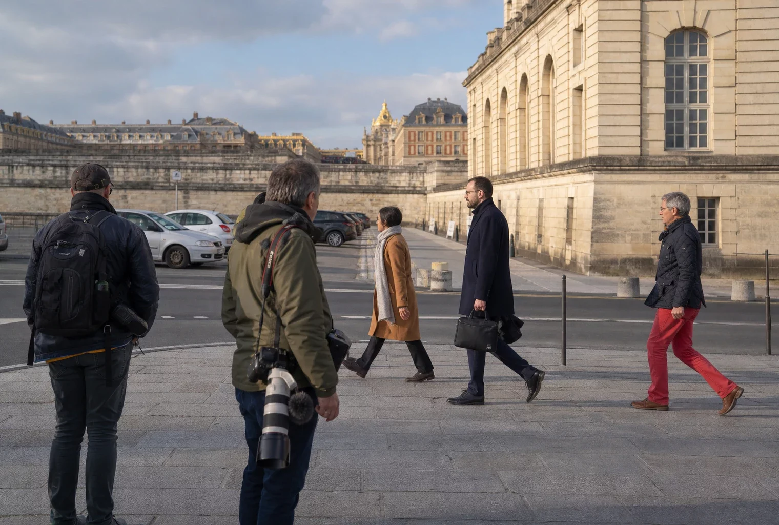 Reportage à Versailles avec passants, photographes de presse et façades du château sous une lumière claire.