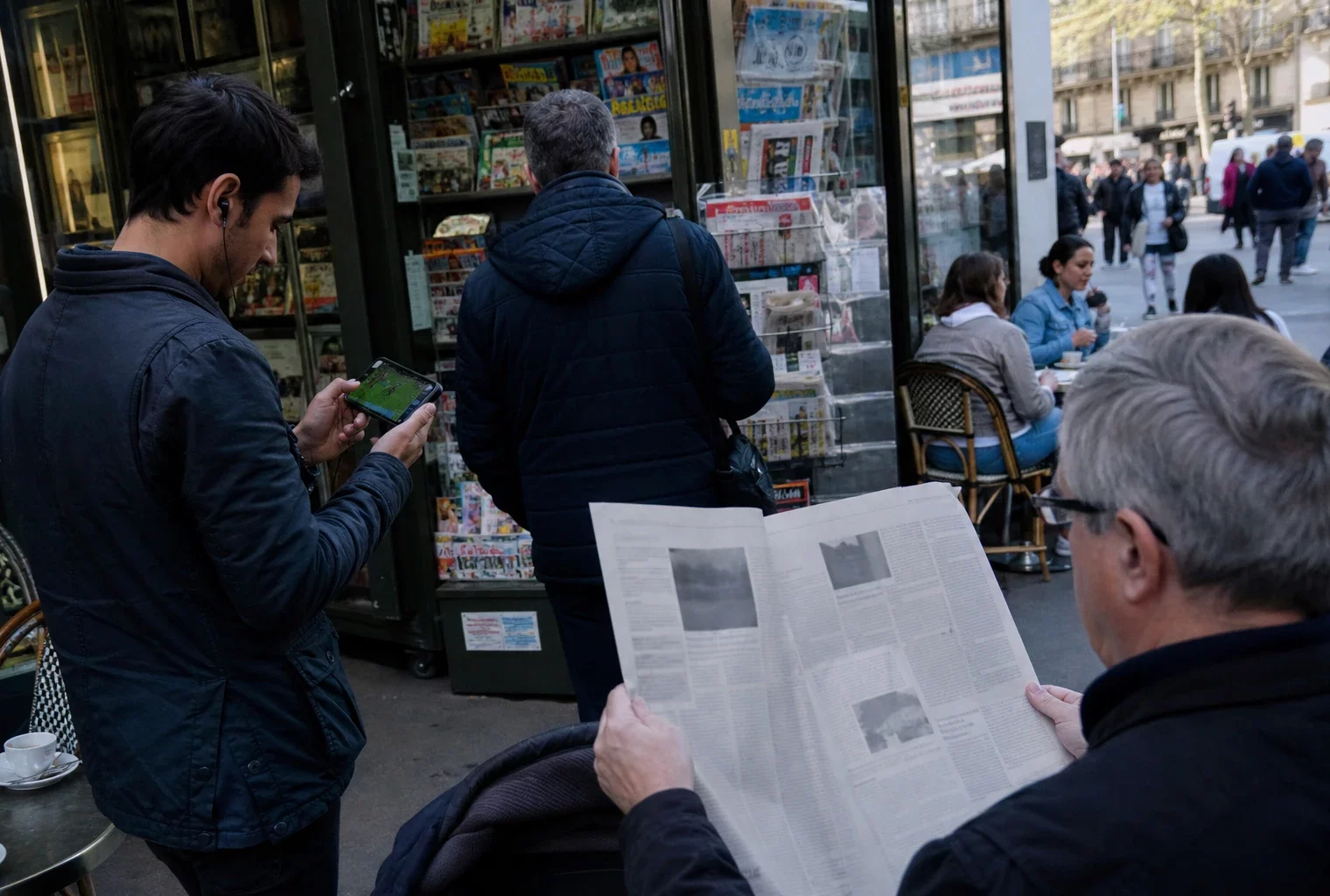 Une scène de vie quotidienne dans une ville française, avec passants, café de quartier et journal tenu en main.
