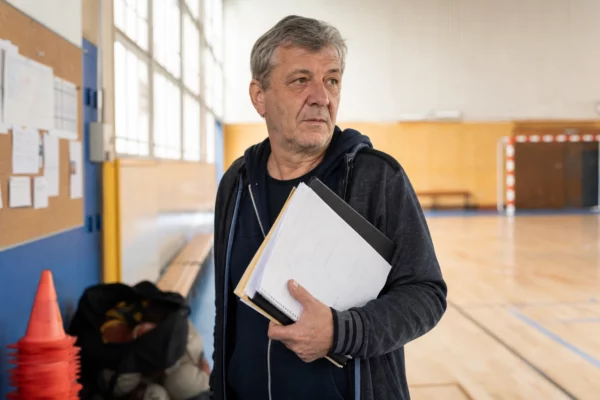 Portrait d’un bénévole anonyme dans un club sportif local, carnet en main, dans une lumière naturelle et chaleureuse.
