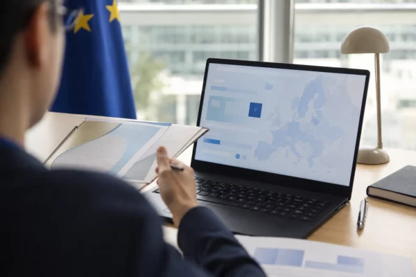 Vue de dos sur un écran d’ordinateur affichant une interface européenne abstraite, dans un bureau lumineux