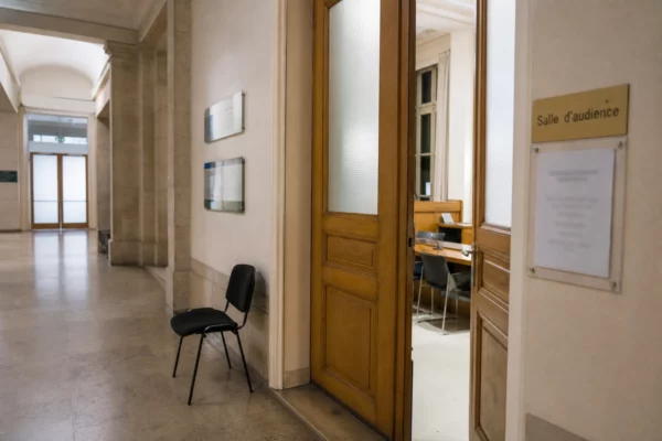 Couloir clair d’un bâtiment institutionnel français avec porte entrouverte vers une salle d’audition, lumière naturelle.