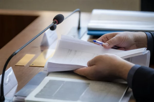 Mains anonymes consultant un dossier en commission avec micro de table dans une lumière claire et naturelle.