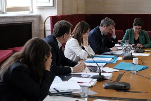 Députés anonymes en commission à l’Assemblée nationale, autour de microphones et dossiers, dans une ambiance de vote fragmenté.
