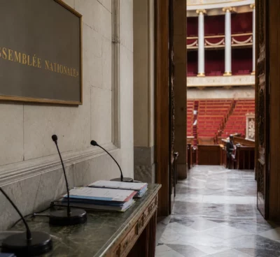 Couloir vide de l’Assemblée nationale avec marbre, velours rouge et micros, en lumière naturelle claire.