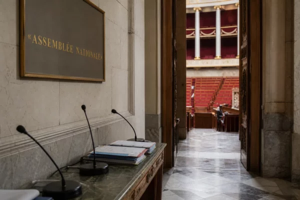 Couloir vide de l’Assemblée nationale avec marbre, velours rouge et micros, en lumière naturelle claire.