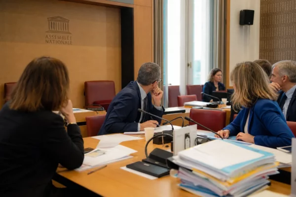 Audition parlementaire sur le budget de la culture avec micros, dossiers ouverts et silhouettes anonymes autour d’une table.
