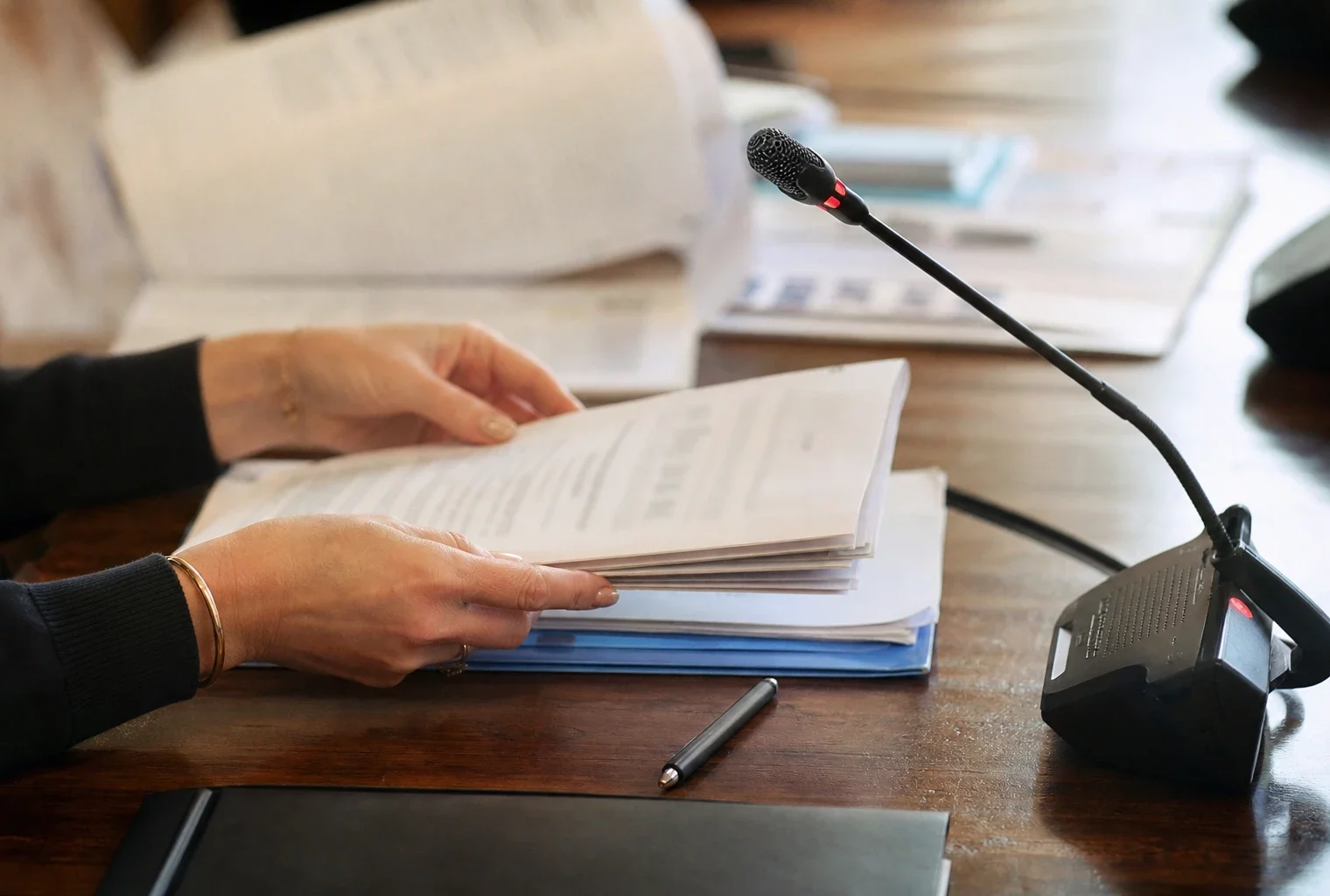 Mains anonymes autour d’un micro de commission et d’un dossier parlementaire flou dans une salle d’audition