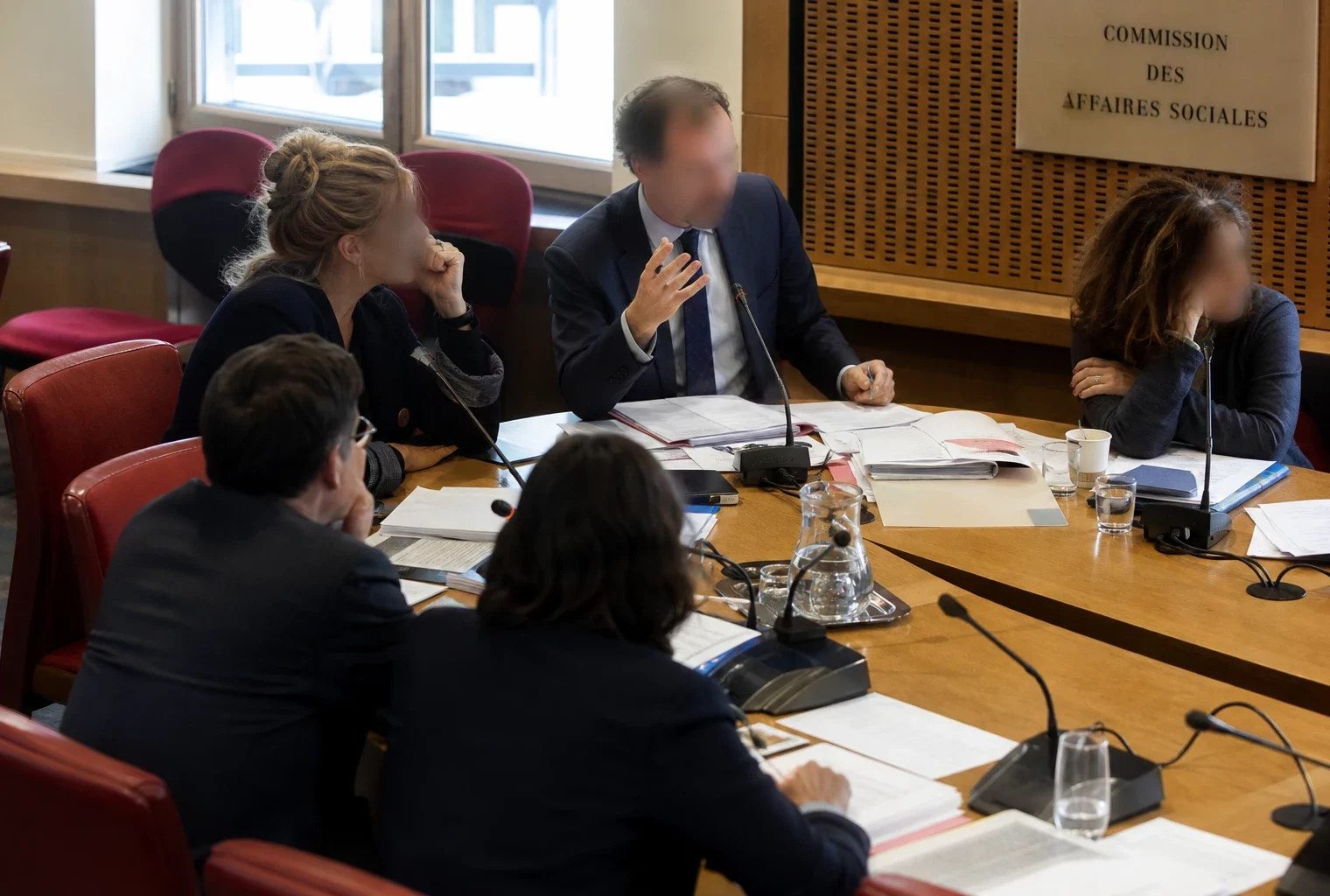 Audition parlementaire en commission avec micros, dossiers ouverts et élus anonymes dans une salle lumineuse