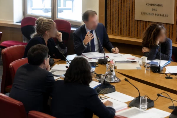 Audition parlementaire en commission avec micros, dossiers ouverts et élus anonymes dans une salle lumineuse