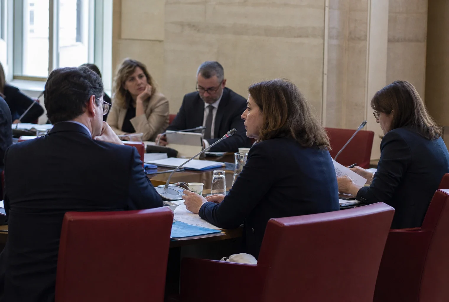 Audition parlementaire en commission avec micros, dossiers ouverts et silhouettes anonymes dans une salle institutionnelle