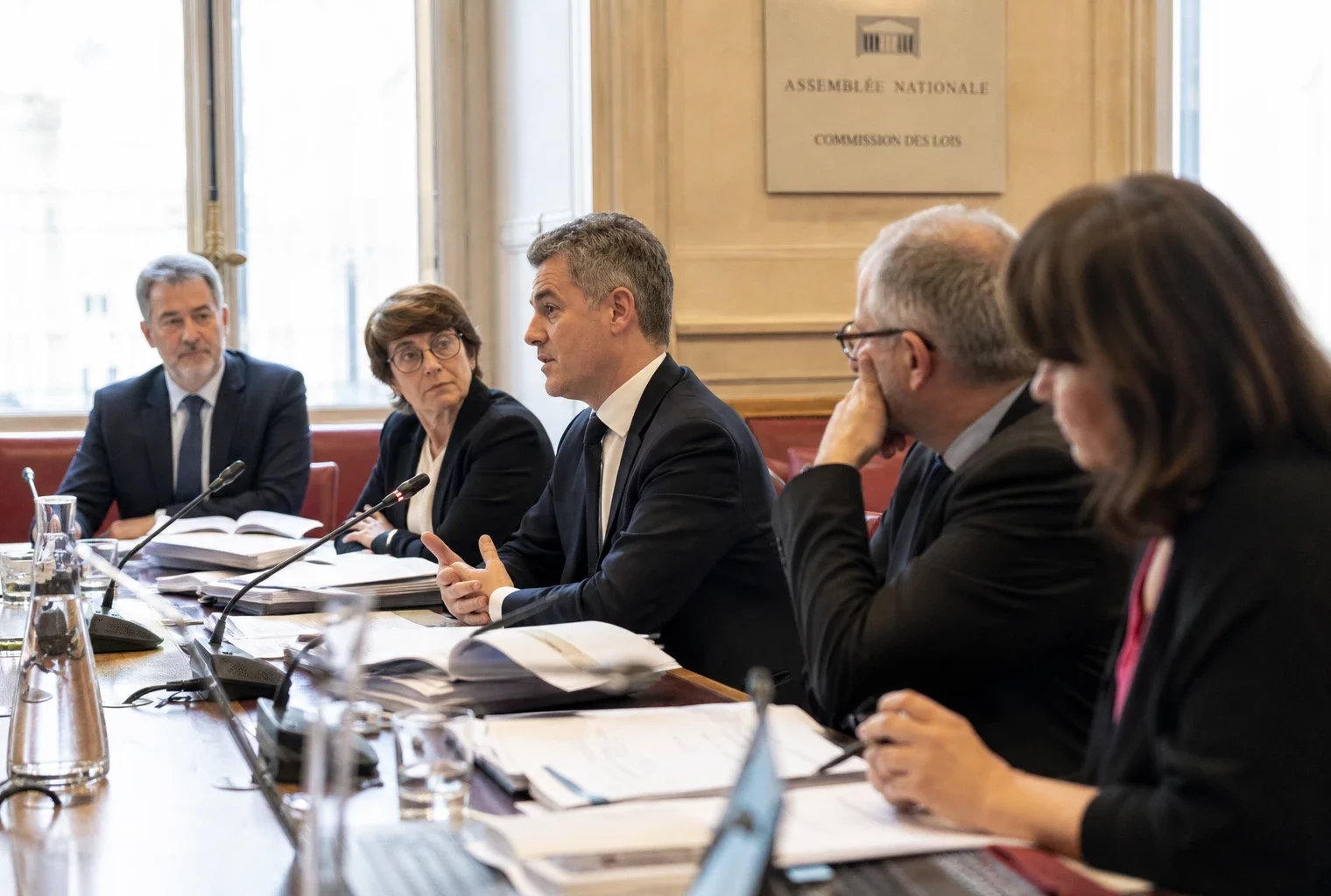 Audition parlementaire sur le Défenseur des droits, avec micros, dossiers ouverts et silhouettes anonymes en commission.