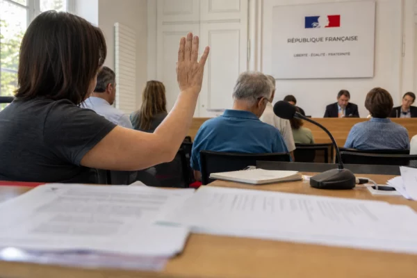 Salle publique d’audition avec micro, documents juridiques flous et main levée dans une ambiance claire et sobre.
