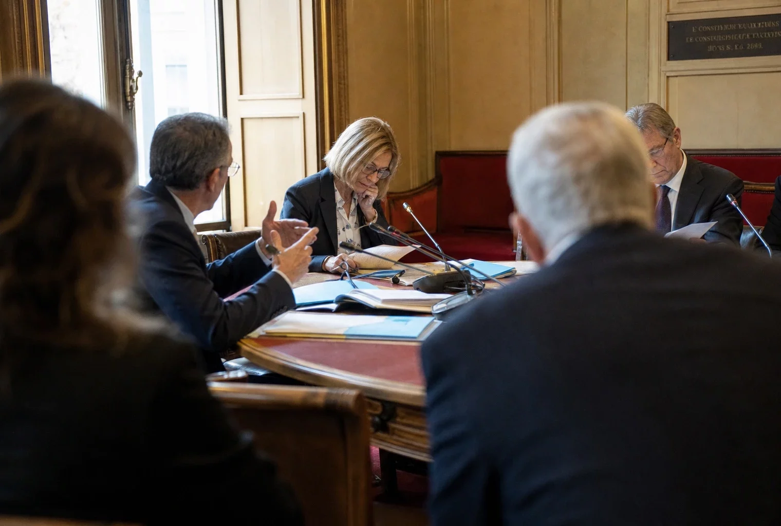 Réunion de commission parlementaire sur l’aide à mourir, avec micros, dossiers et silhouettes anonymes en salle claire.