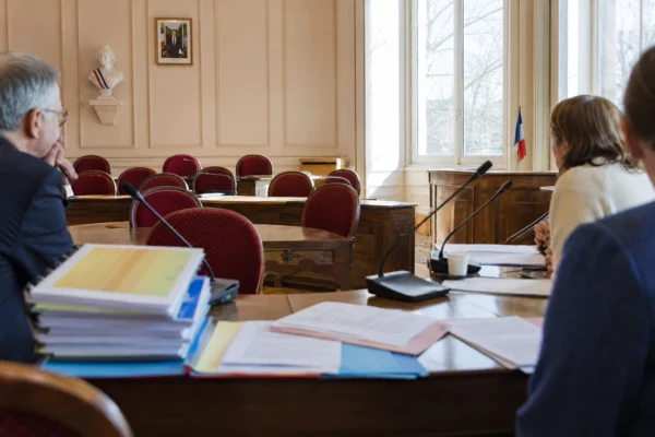 Salle municipale avec micros, dossiers et chaise vide symbolisant l’avocat automatique pour les enfants protégés.