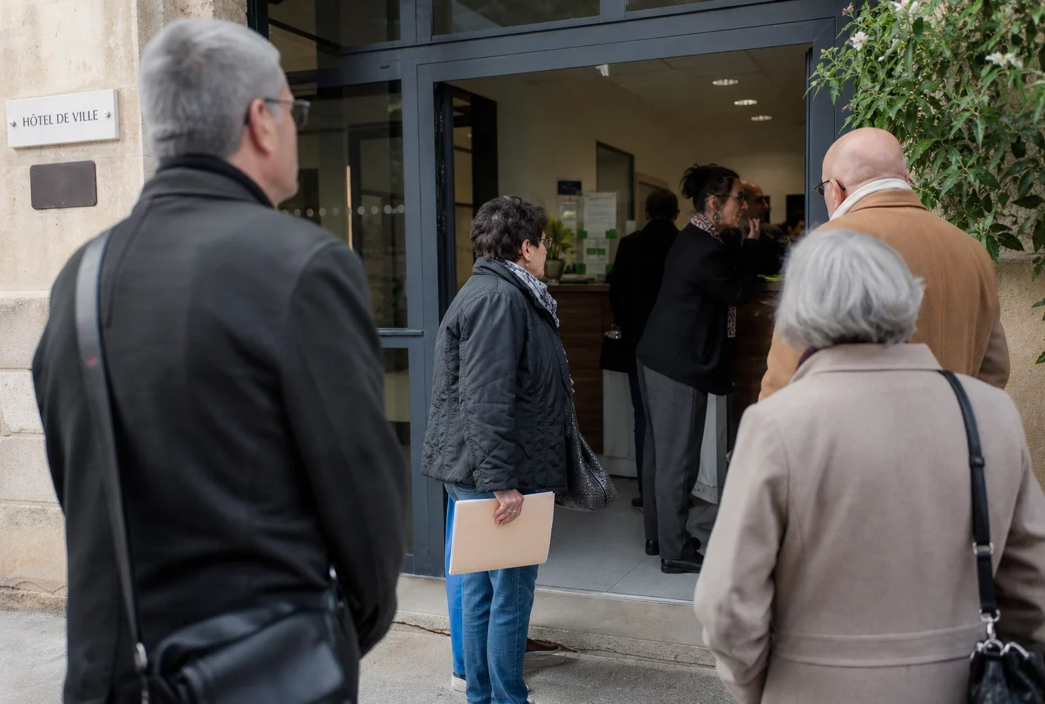 Des habitants anonymes attendent devant une mairie de ville française, dans une scène de service public lumineuse.