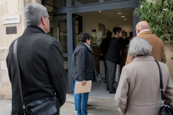 Des habitants anonymes attendent devant une mairie de ville française, dans une scène de service public lumineuse.