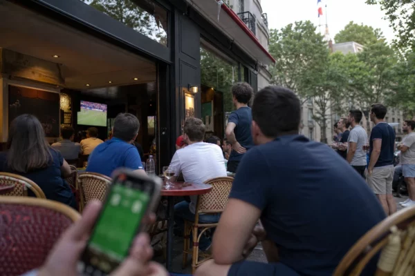 Supporters français dans un café de quartier regardant la finale de la Coupe du monde sur un écran intérieur.
