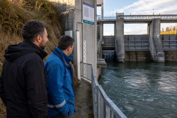 Un ingénieur et un technicien observent un barrage hydroélectrique français au bord d’une rivière, en lumière naturelle.