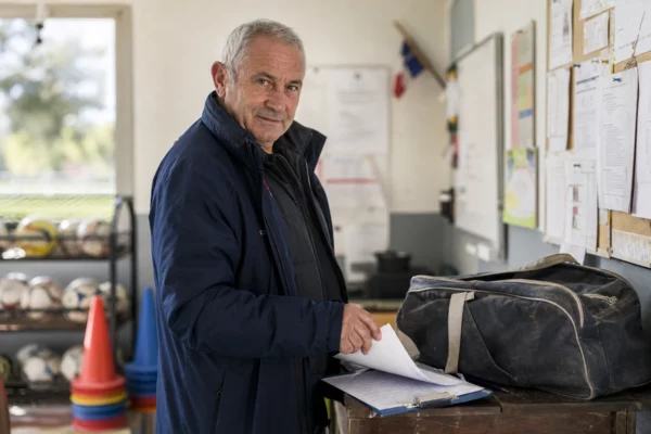 Bénévole de club de football dans un local municipal, avec clipboard et matériel sportif, en portrait naturel