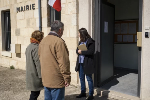 Des habitants devant une mairie de petite ville discutent d’un projet local sous un budget public
