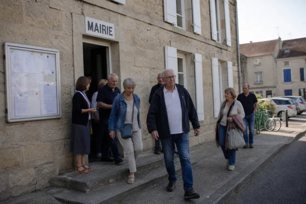 Des habitants quittent une mairie de village après une réunion locale, dans une lumière claire et naturelle.