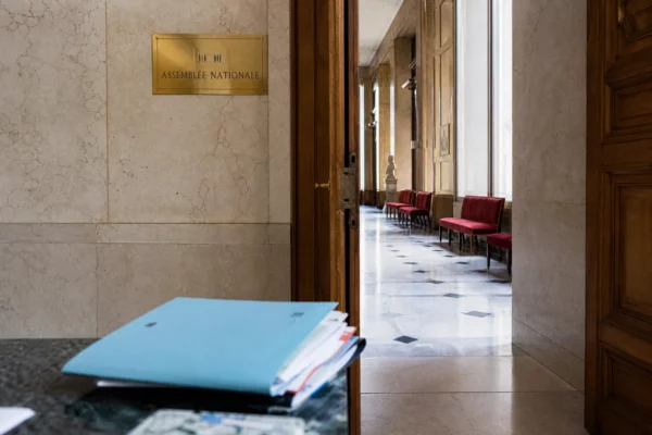 Couloir de l’Assemblée nationale avec dossiers budgétaires flous et lumière naturelle, scène institutionnelle vide.