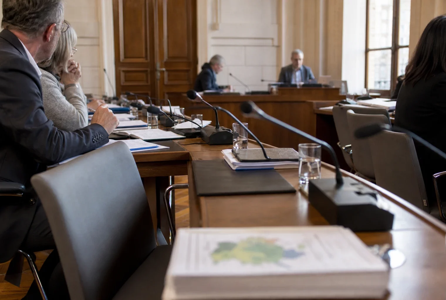 Salle municipale lumineuse avec chaises vides, micros et dossiers flous pour illustrer le budget écologie.