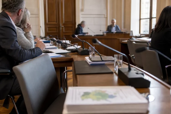 Salle municipale lumineuse avec chaises vides, micros et dossiers flous pour illustrer le budget écologie.