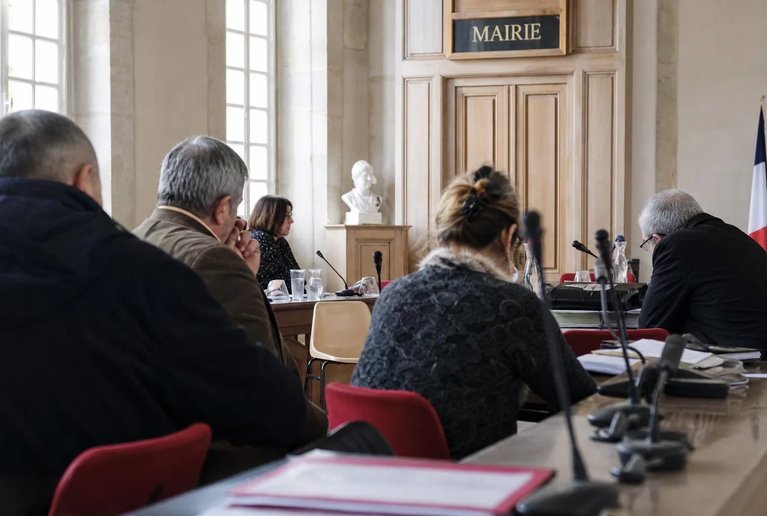 Salle municipale française avec micros et dossiers flous, chaise vide et ambiance de conseil local