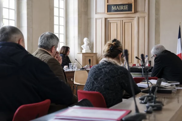 Salle municipale française avec micros et dossiers flous, chaise vide et ambiance de conseil local