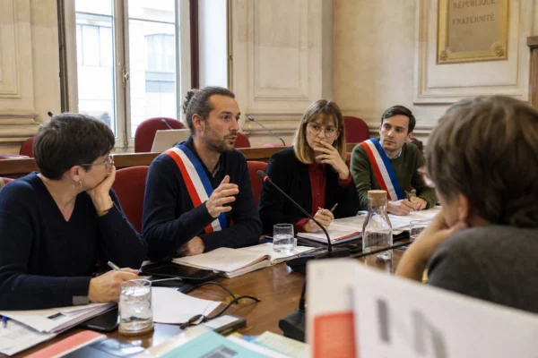 Réunion institutionnelle de plusieurs élus et collaborateurs autour d’une table, avec micros et dossiers dans une salle lumineuse.