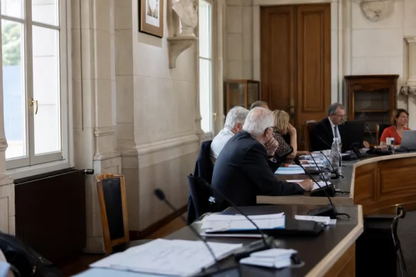 Salle municipale lumineuse avec chaise vide, micros et dossiers flous lors d’une réunion locale sur la canicule.