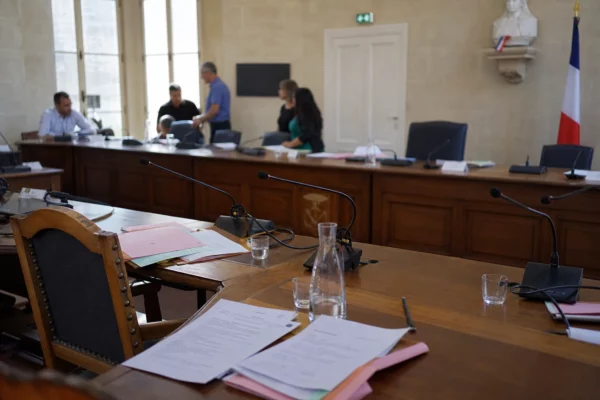 Salle municipale française avec micros, dossiers et chaise vide après une réunion sur la canicule.