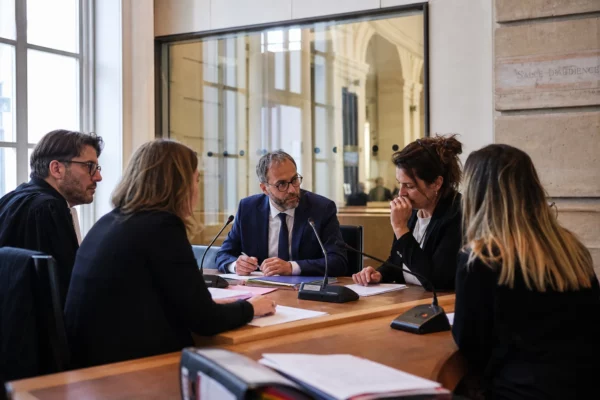 Réunion institutionnelle au palais de justice avec cinq personnes anonymes autour d’une table et des dossiers ouverts.