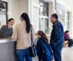 Des habitants anonymes discutent dans le hall lumineux d’une mairie française avec un enfant en cartable.
